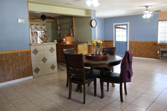 dining space with wooden walls, ceiling fan, wainscoting, and light tile patterned flooring
