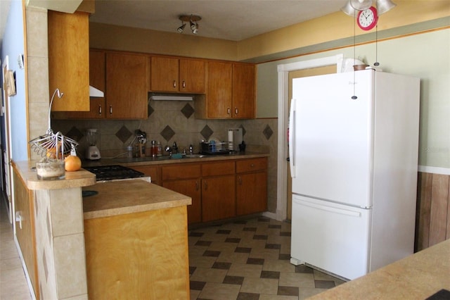 kitchen with brown cabinets, backsplash, light countertops, and freestanding refrigerator