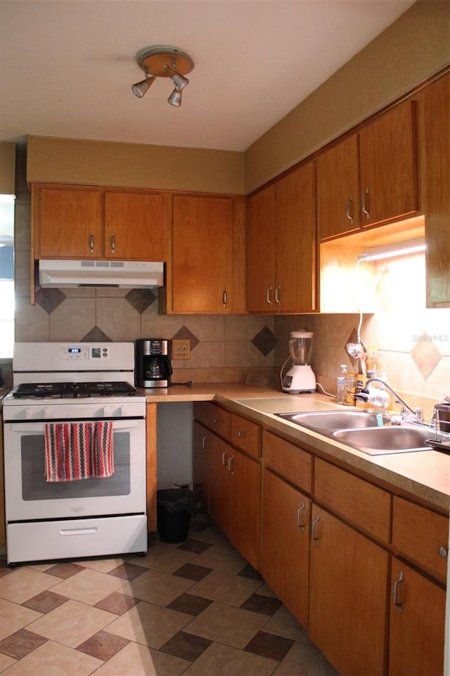 kitchen with a sink, light countertops, gas range gas stove, under cabinet range hood, and decorative backsplash