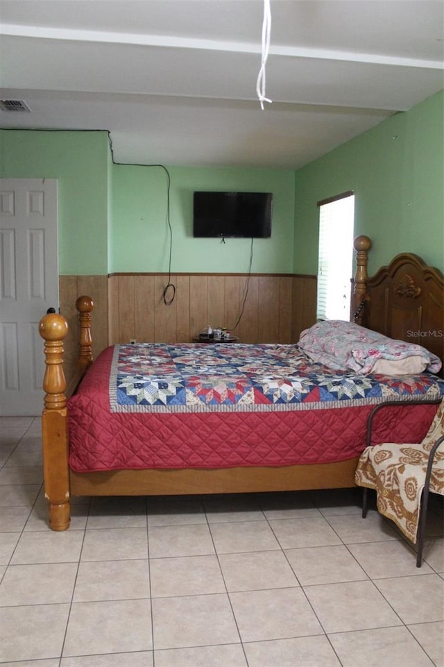 bedroom featuring light tile patterned floors, visible vents, and a wainscoted wall
