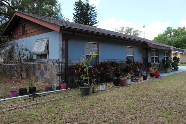 back of property featuring a yard, roof with shingles, and stucco siding