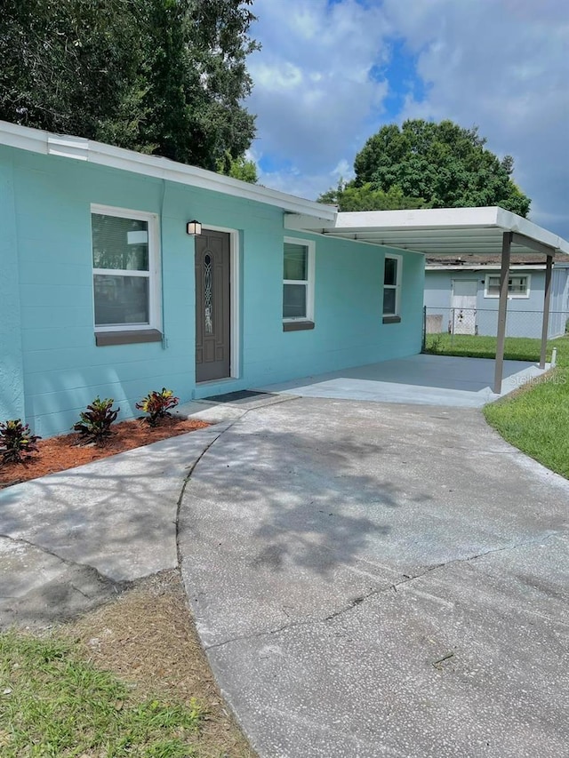 ranch-style house featuring concrete block siding, fence, and an attached carport