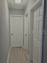 hall featuring baseboards, attic access, and wood finished floors