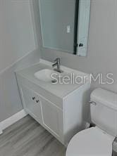 half bath with vanity, baseboards, toilet, and wood finished floors