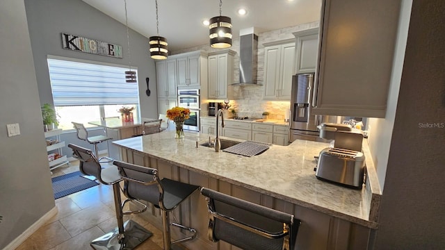 kitchen with a peninsula, appliances with stainless steel finishes, light stone counters, a breakfast bar area, and wall chimney range hood