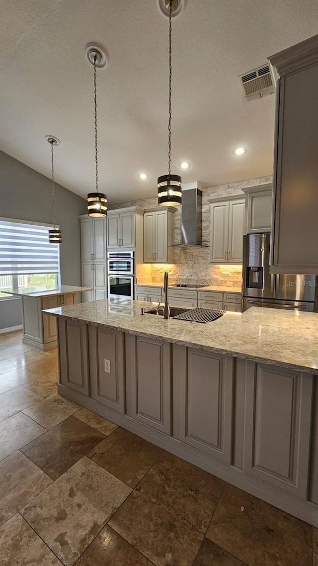 kitchen with gray cabinets, stainless steel appliances, backsplash, visible vents, and wall chimney range hood