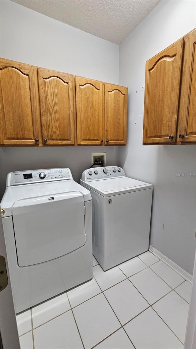 laundry room featuring washer and clothes dryer, baseboards, a textured ceiling, light tile patterned flooring, and cabinet space