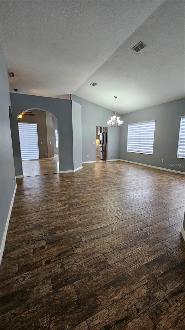 unfurnished living room featuring dark wood-style flooring, a notable chandelier, vaulted ceiling, and visible vents