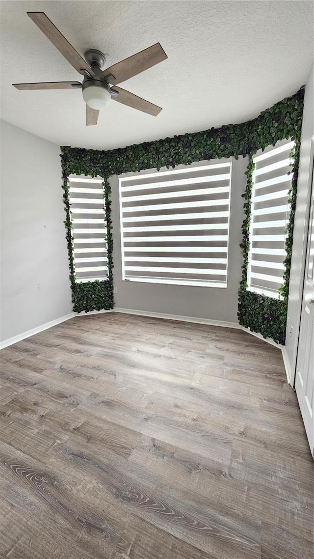 unfurnished room with a ceiling fan, wood finished floors, baseboards, and a textured ceiling