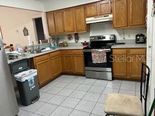 133 Bianca Ct, Kissimmee, FL 34758 - kitchen featuring light countertops, stainless steel range with electric stovetop, light tile patterned floors, under cabinet range hood, and brown cabinets