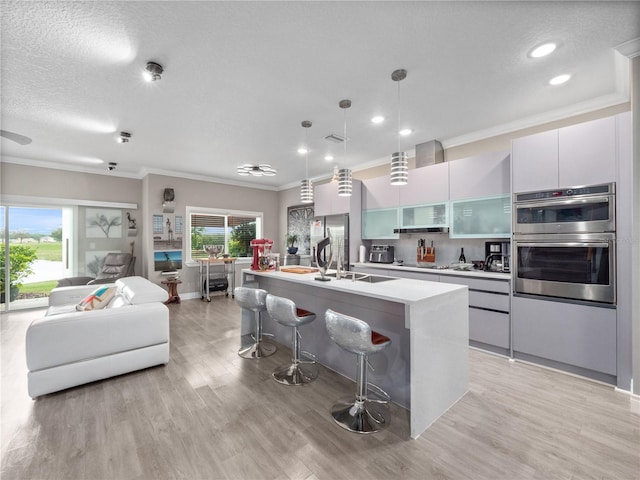 1911 Greenbriar Ter, Davenport, FL 33837 - kitchen featuring crown molding, a kitchen island with sink, light wood-style floors, a breakfast bar area, and double oven