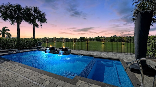 pool at dusk with fence, a patio area, a pool with connected hot tub, and an outdoor fire pit