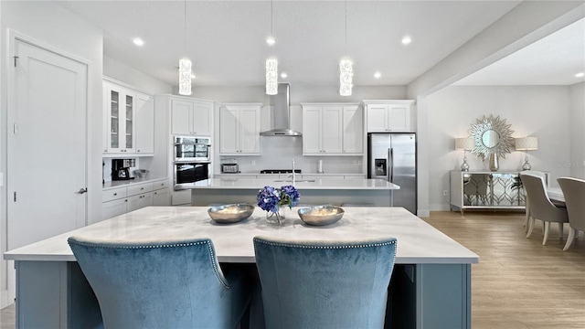 kitchen with wall chimney range hood, stainless steel appliances, light countertops, and a kitchen island with sink