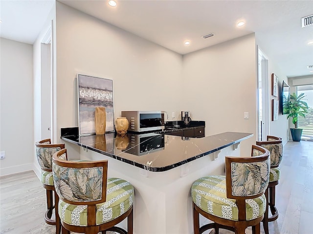interior space featuring a kitchen breakfast bar, stainless steel microwave, baseboards, recessed lighting, and wood finished floors