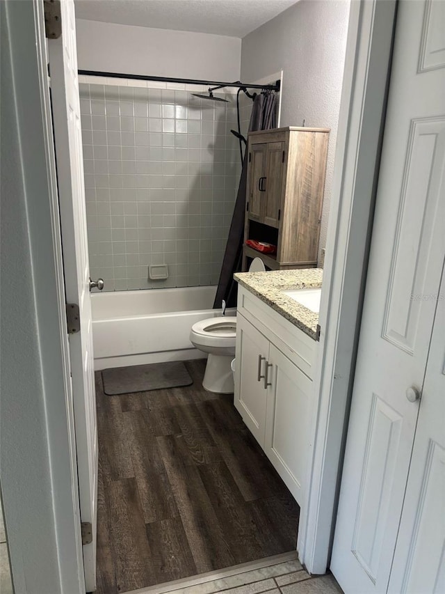 bathroom with wood finished floors, toilet, vanity, shower / tub combo, and a textured wall
