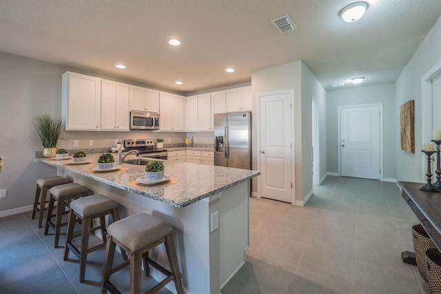 848 San Pedro Ct, Kissimmee, FL 34758 - kitchen featuring visible vents, appliances with stainless steel finishes, a breakfast bar, a peninsula, and light stone counters