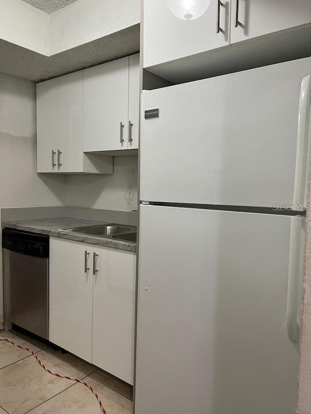 kitchen with light tile patterned floors, white cabinetry, freestanding refrigerator, dishwasher, and a sink