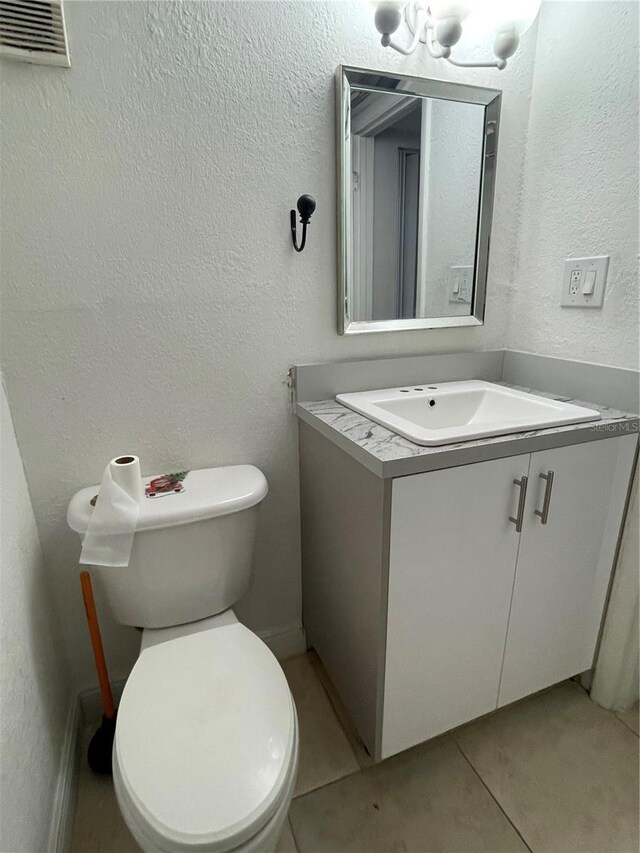 bathroom featuring tile patterned flooring, toilet, vanity, and a textured wall