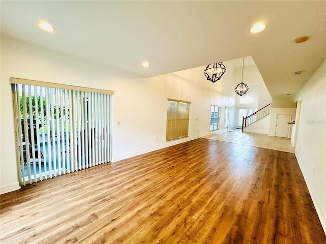 unfurnished living room with baseboards, a notable chandelier, stairway, recessed lighting, and wood finished floors