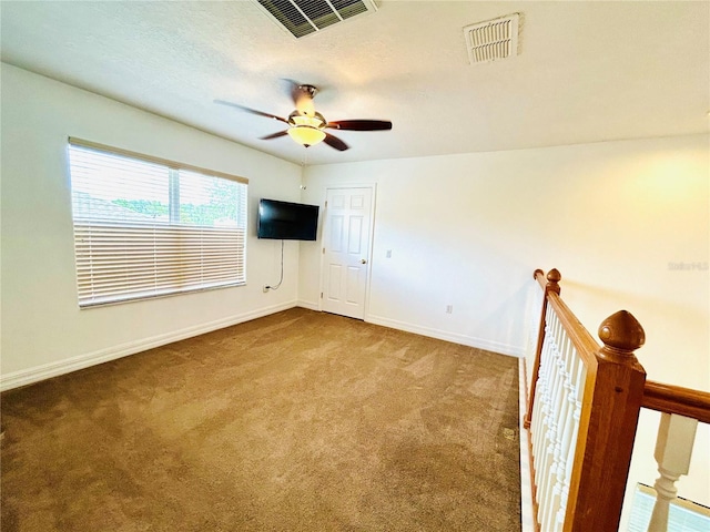 carpeted spare room with visible vents, ceiling fan, baseboards, and a textured ceiling