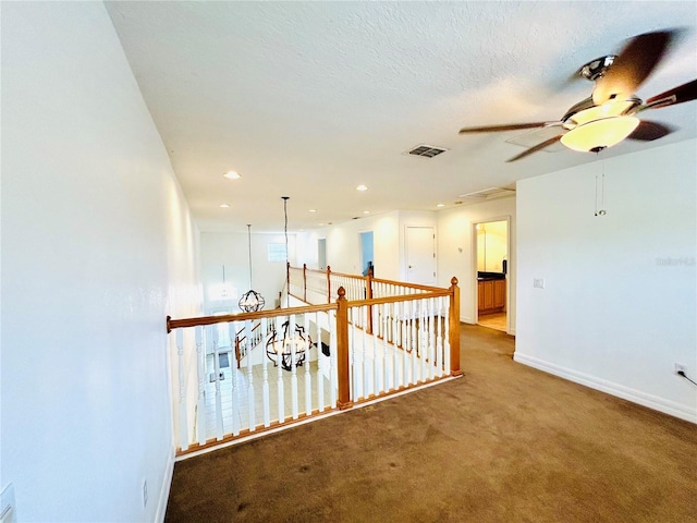hall with a textured ceiling, visible vents, recessed lighting, carpet flooring, and baseboards