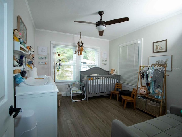 bedroom featuring a crib, ornamental molding, a ceiling fan, and wood finished floors