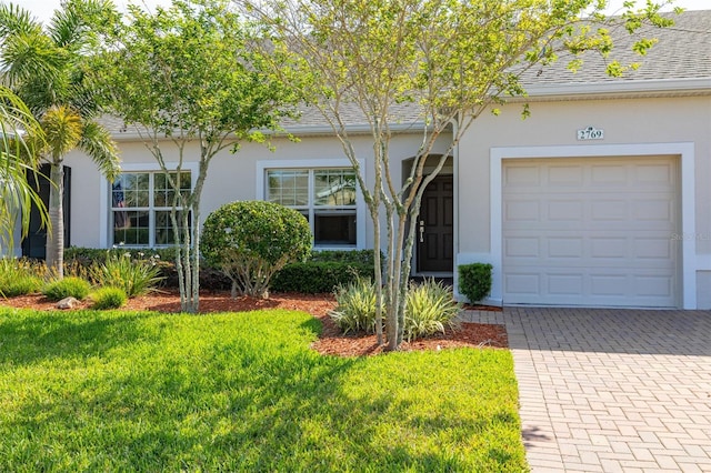 single story home featuring a garage, stucco siding, a front lawn, decorative driveway, and roof with shingles