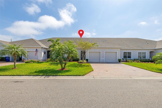 ranch-style house with an attached garage, stucco siding, a front lawn, and decorative driveway