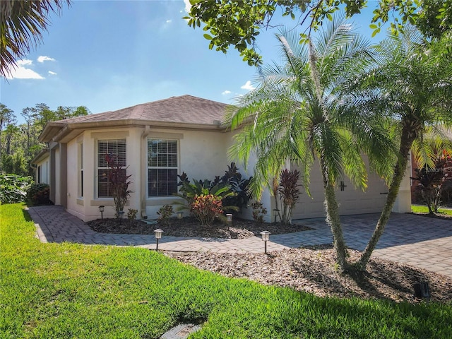 524 Grand Canal Dr, Poinciana, FL 34759 - view of side of home with roof with shingles, stucco siding, decorative driveway, an attached garage, and a lawn