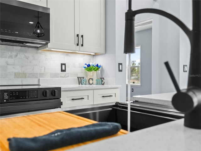 145 Willow Dr, Poinciana, FL 34759 - kitchen with stainless steel microwave, tasteful backsplash, light stone counters, white cabinetry, and black electric range