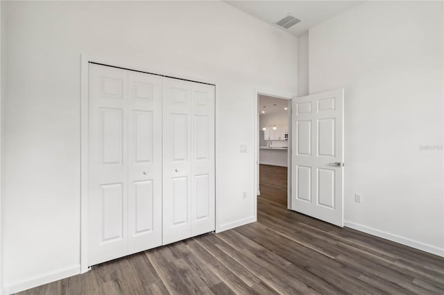 unfurnished bedroom with a towering ceiling, a closet, baseboards, dark wood-style floors, and visible vents