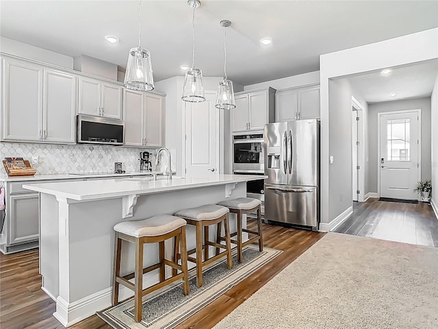 kitchen featuring a sink, stainless steel appliances, light countertops, backsplash, and dark wood-type flooring