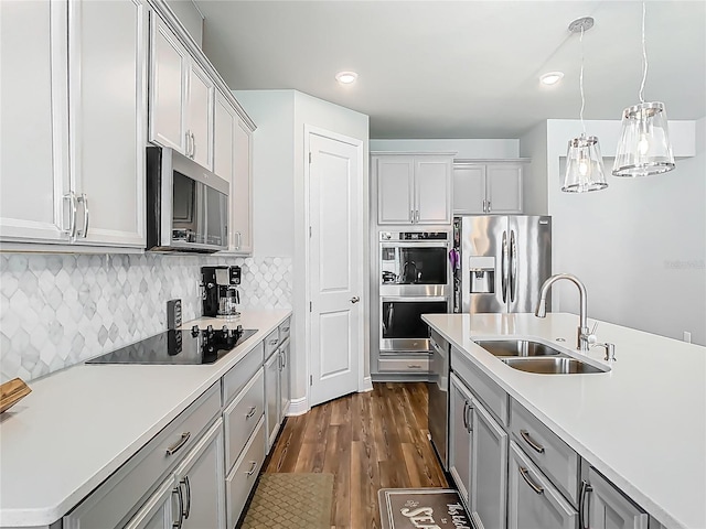 kitchen with hanging light fixtures, a sink, stainless steel appliances, light countertops, and dark wood-style floors