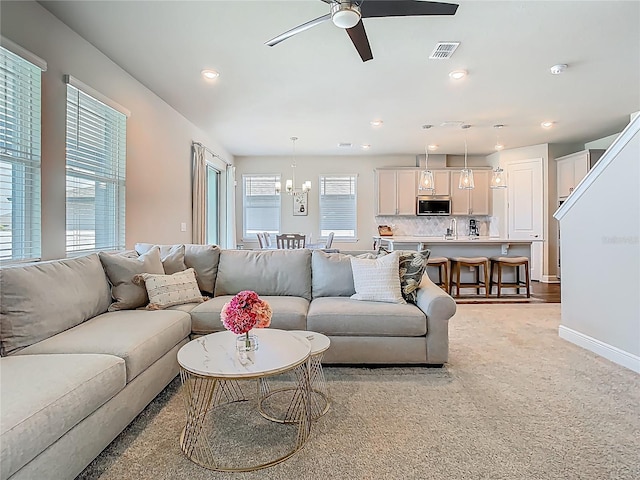 living room featuring ceiling fan with notable chandelier, light colored carpet, baseboards, visible vents, and recessed lighting