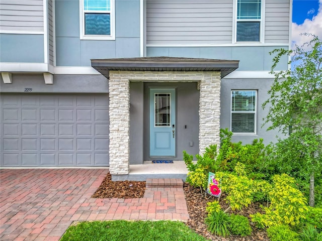 entrance to property with stucco siding, an attached garage, decorative driveway, and stone siding