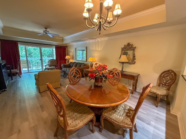 dining area with a tray ceiling, ornamental molding, ceiling fan with notable chandelier, and wood finished floors