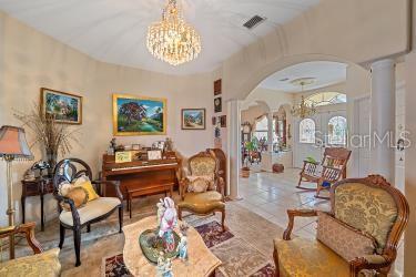 18011 Prairie Wolf Gln, Parrish, FL 34219 - living area featuring tile patterned flooring, arched walkways, a chandelier, decorative columns, and visible vents
