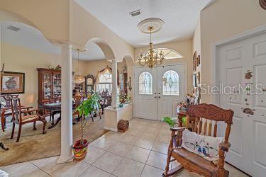 18011 Prairie Wolf Gln, Parrish, FL 34219 - entrance foyer featuring arched walkways, a chandelier, french doors, light tile patterned floors, and ornate columns