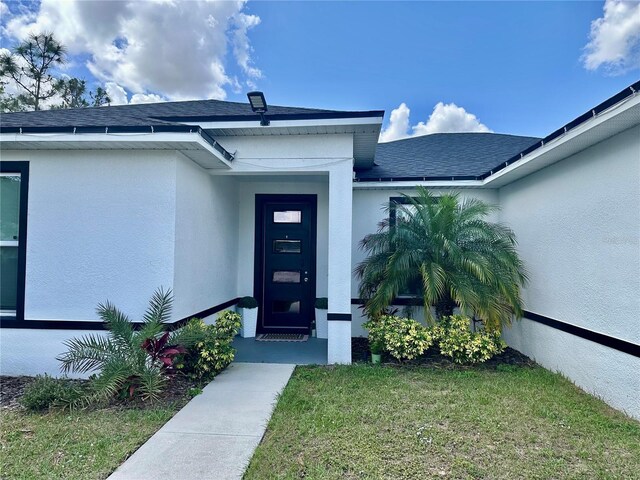 1804 Hudson Ct, Poinciana, FL 34759 - property entrance with roof with shingles, a yard, and stucco siding