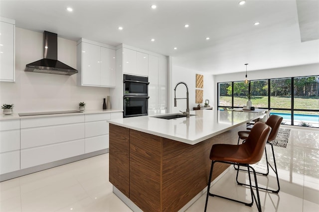 kitchen with white cabinetry, dobule oven black, wall chimney exhaust hood, modern cabinets, and a sink