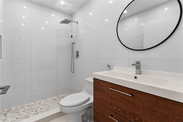 bathroom with a tile shower, tile walls, toilet, and vanity