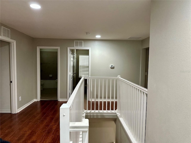 corridor featuring visible vents, baseboards, an upstairs landing, and wood finished floors