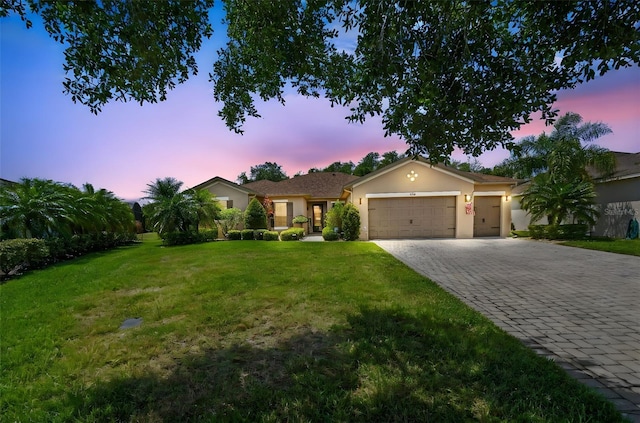 ranch-style home with stucco siding, decorative driveway, a lawn, and a garage