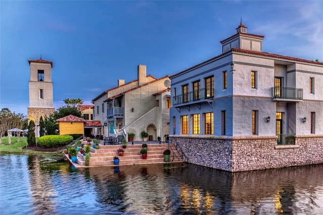 rear view of property with stairway, a balcony, a water view, cooling unit, and a chimney