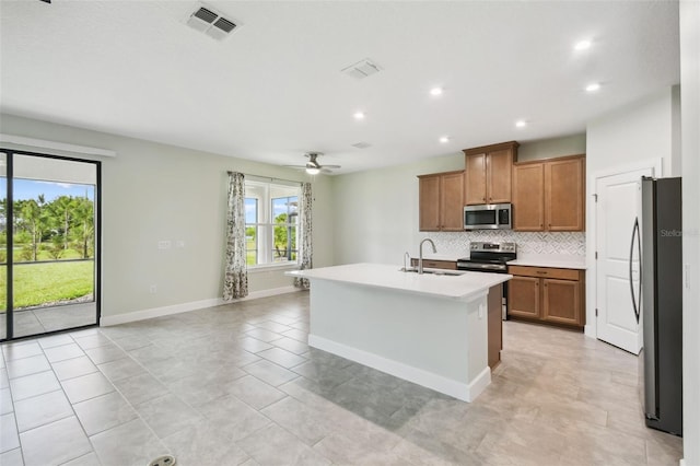 204 Bella Cortina Dr, Kissimmee, FL 34759 - kitchen with appliances with stainless steel finishes, a sink, tasteful backsplash, brown cabinetry, and an island with sink