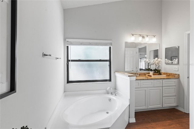 full bathroom featuring a wealth of natural light, vanity, wood finished floors, and a garden tub