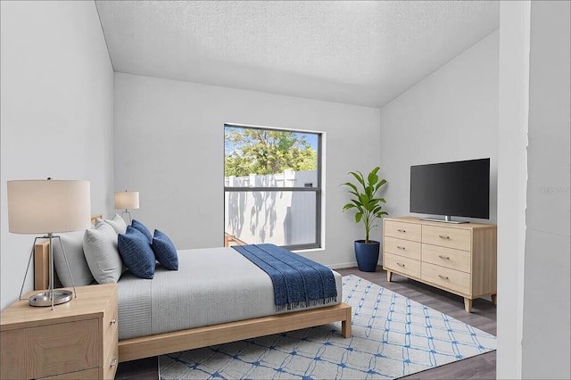 bedroom with vaulted ceiling, a textured ceiling, baseboards, and wood finished floors