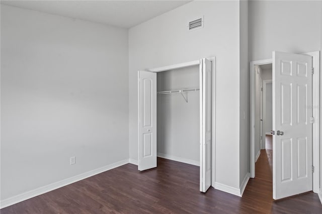 unfurnished bedroom with a closet, baseboards, dark wood finished floors, and visible vents