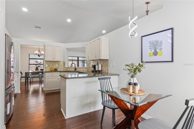 kitchen featuring a peninsula, dark wood-style flooring, a sink, a notable chandelier, and backsplash