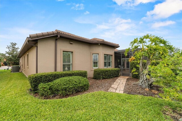 469 Sorrento Rd, Kissimmee, FL 34759 - view of side of home with a yard, a tiled roof, glass enclosure, cooling unit, and stucco siding